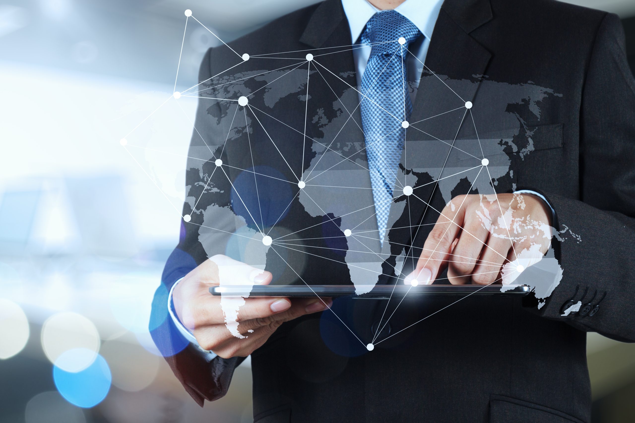 Image of a man's torso wearing a black suit holding a tablet pc. graph of a map of the world is imposed on the image